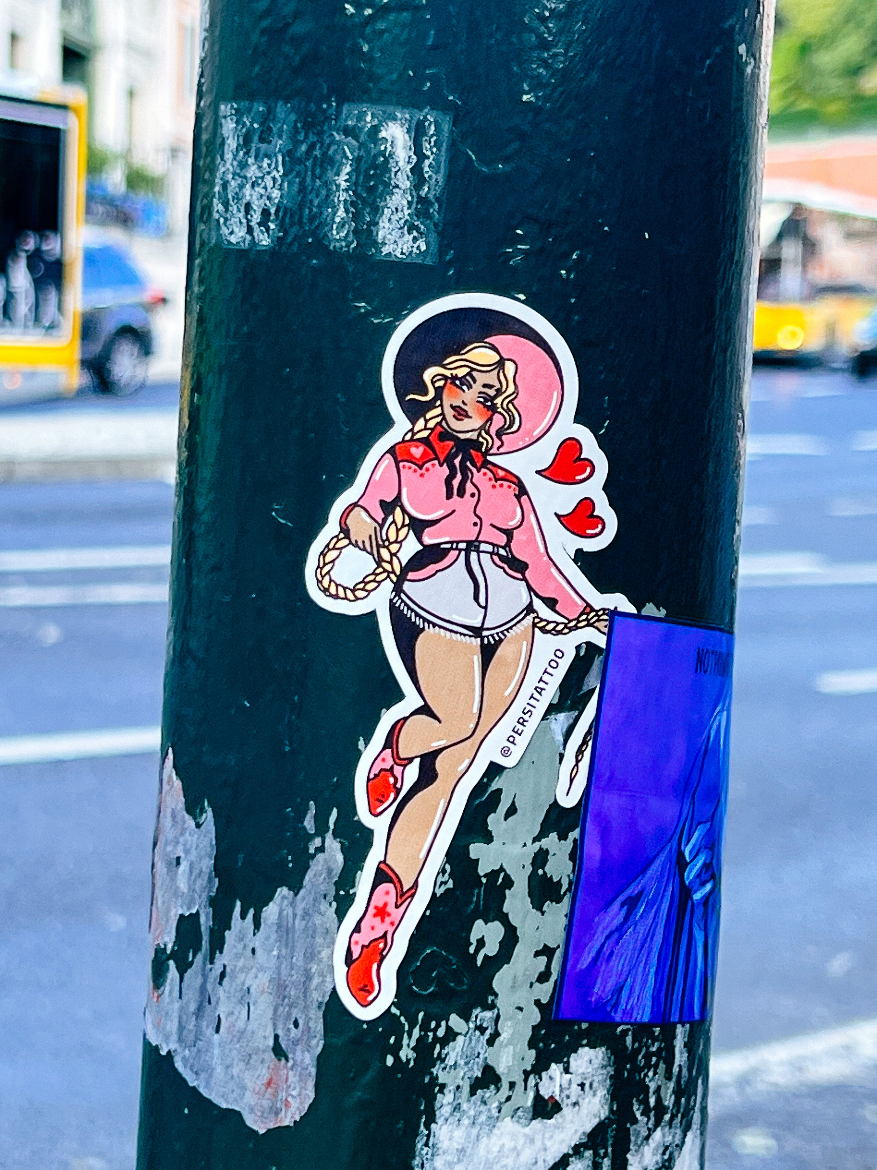 Sticker advertising a tattoo artist, with a drawing of a cowgirl pinup. 