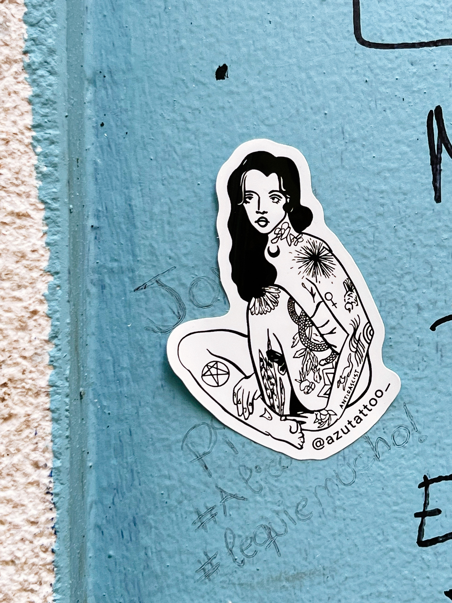 Sticker, drawing of a woman sitting down, body covered with tattoos. 