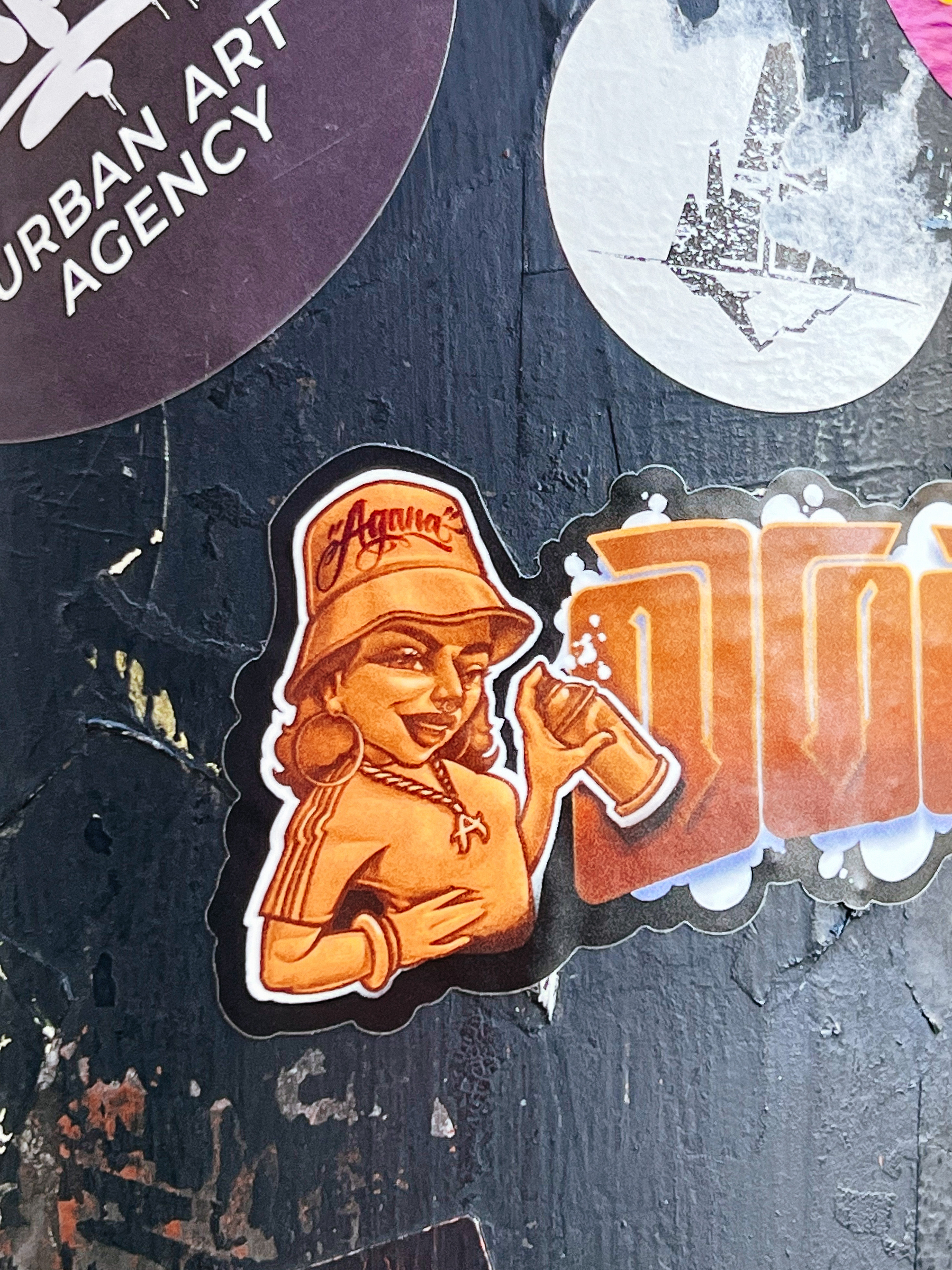 Sticker with the drawing of a girl holding a spray paint can, winking at us.
