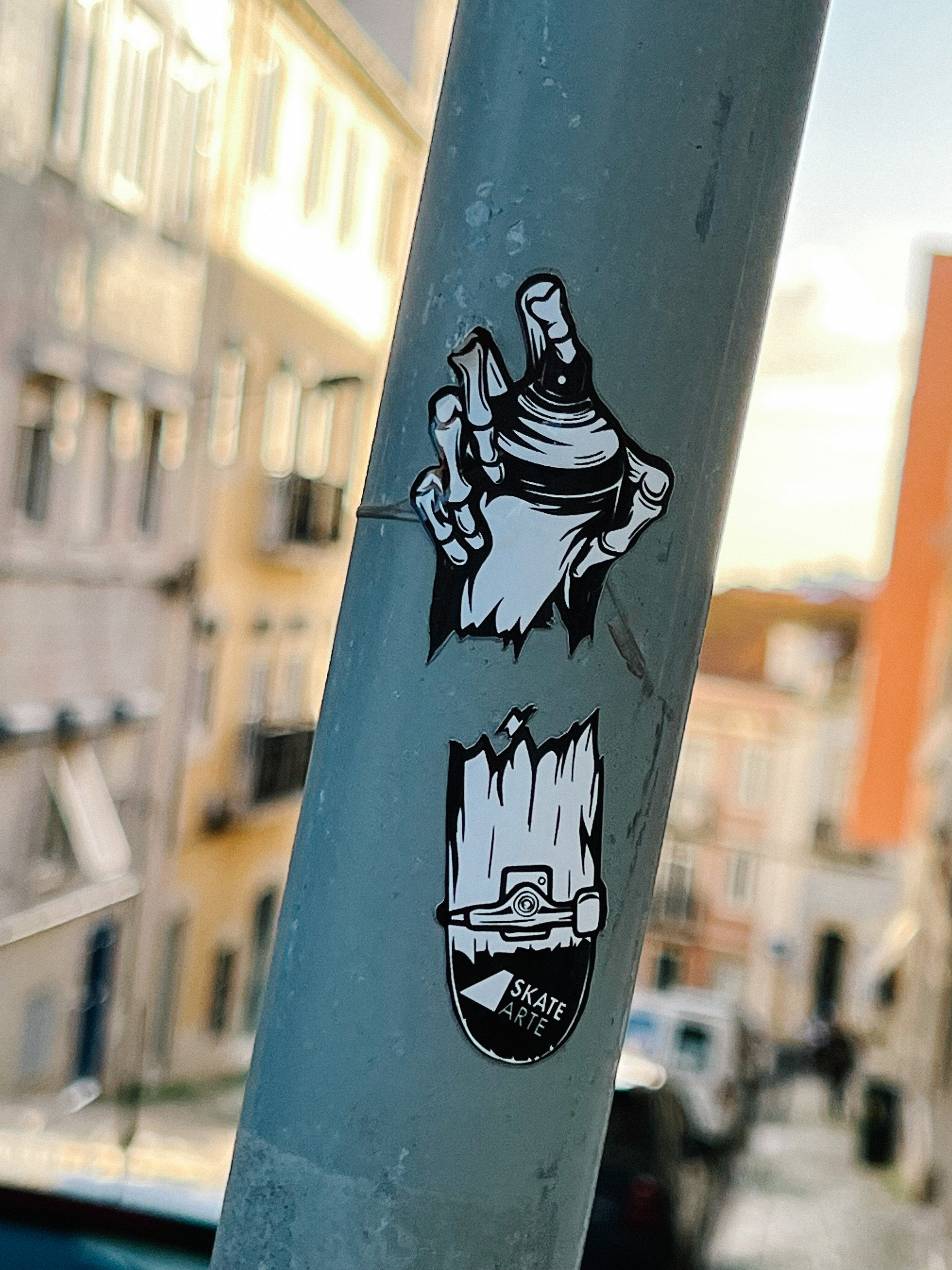 Two part sticker. One hand holding a spray paint can on top, and a broken skateboard on the bottom. 