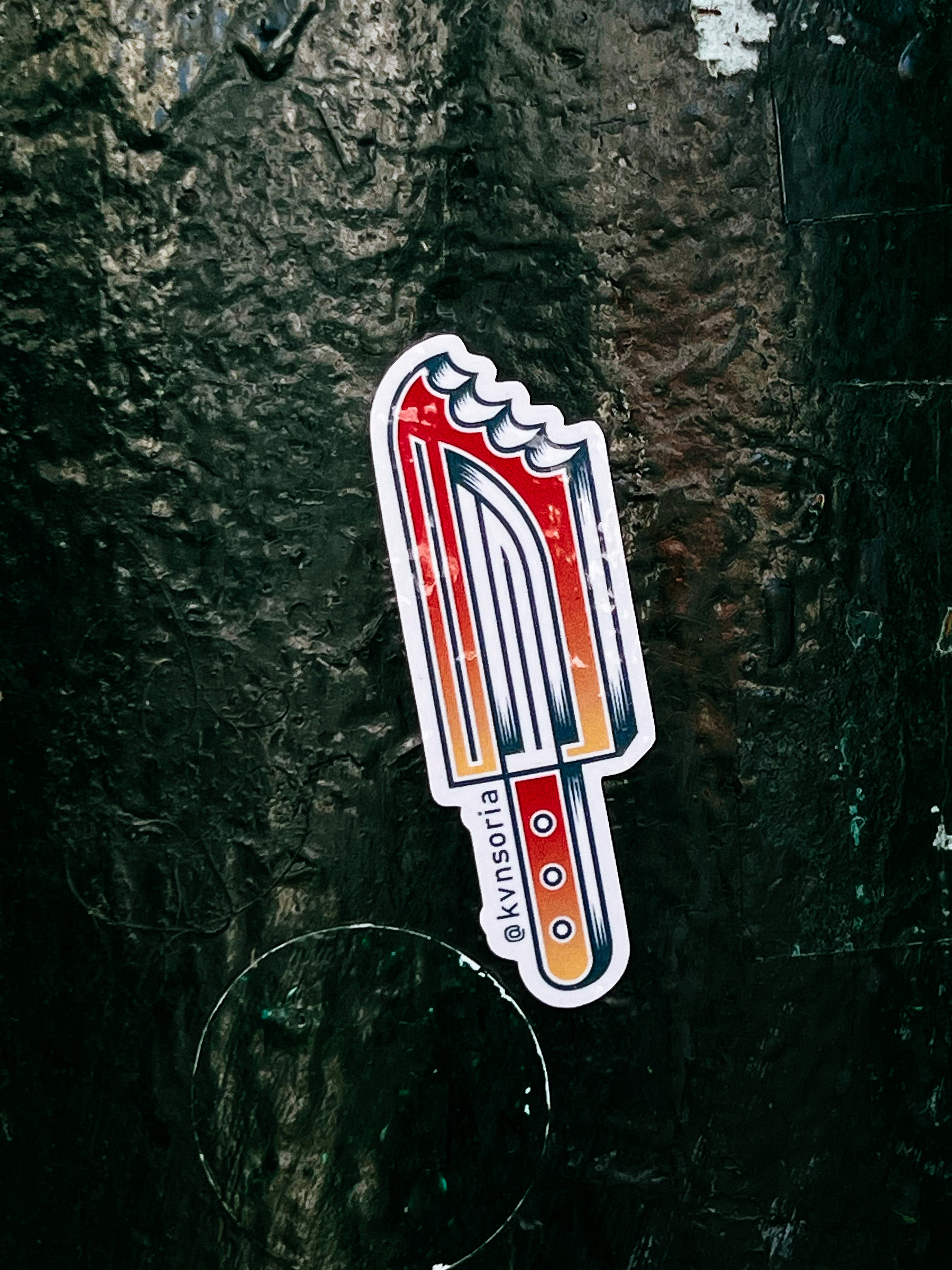 Sticker with a drawing in American classic tattoo style of a popsicle, with a knife handle, and a blade. 