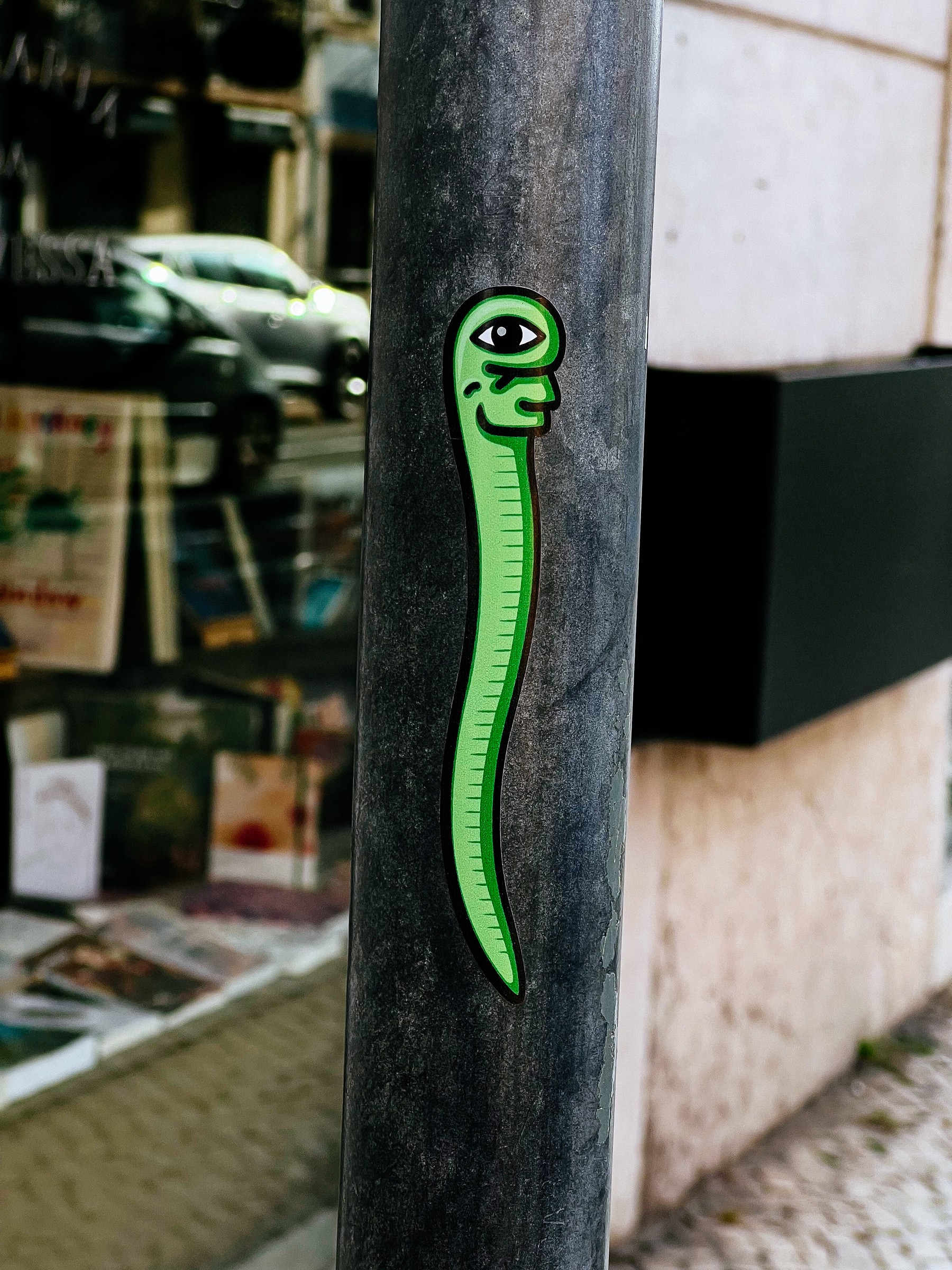 Sticker with a strange looking cartoony snake. Green, with a human like mouth, and one eye. 