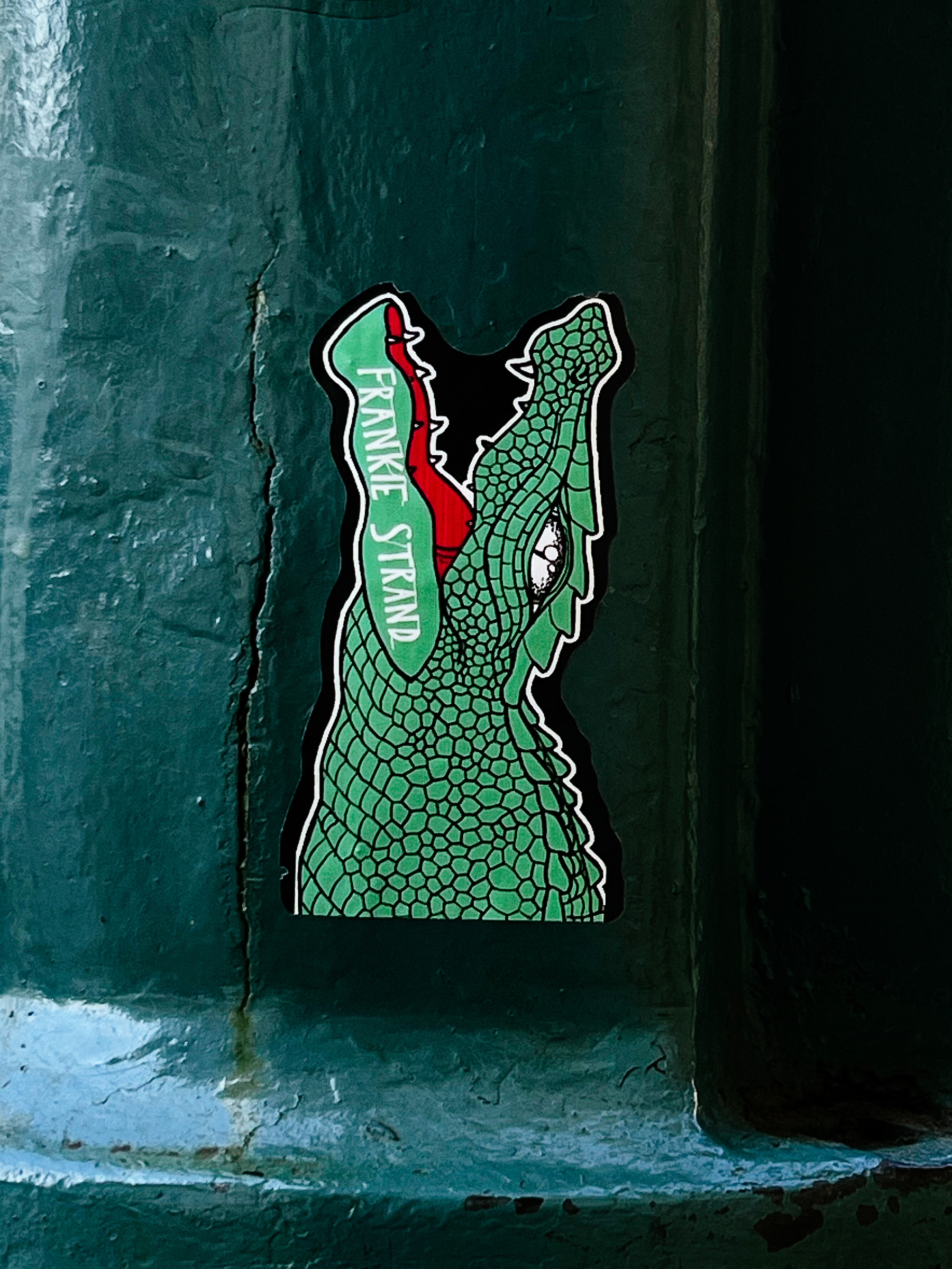 Sticker with a crocodile’s head, mouth open. The name “Frankie Strand” written on it.  