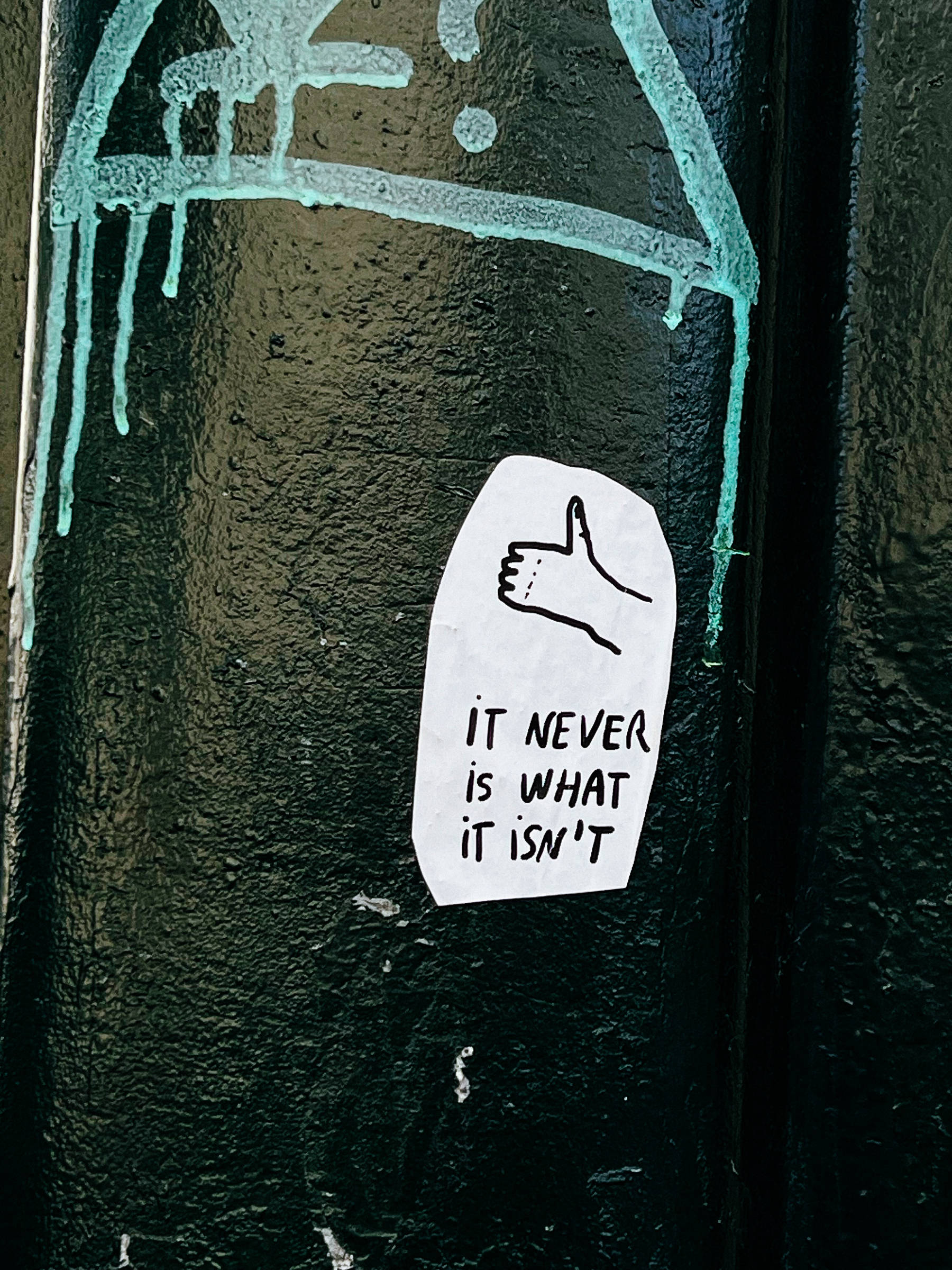 Sticker with a hand doing a &ldquo;thumbs up&rdquo;, and the words &ldquo;IT NEVER IS WHAT IT ISN&rsquo;T&rdquo;. 