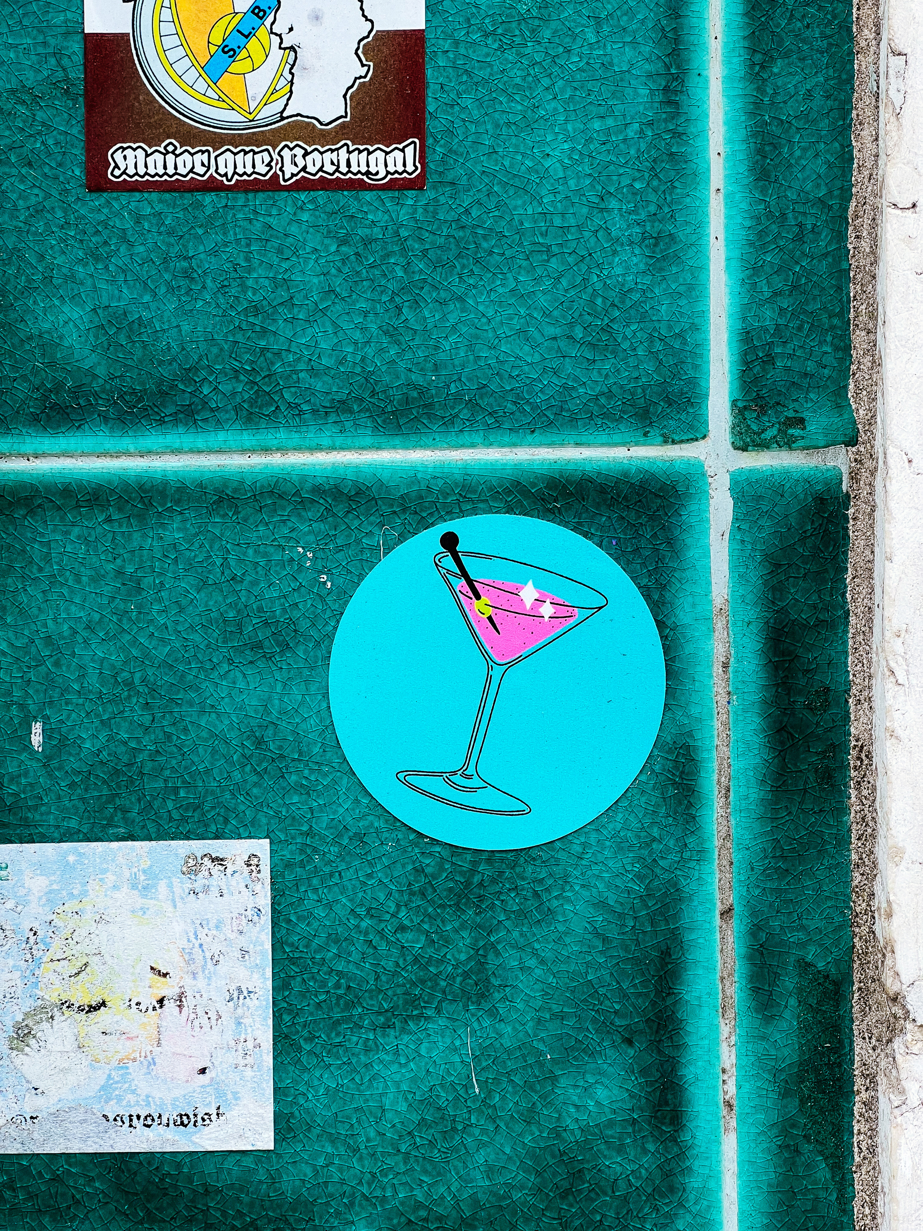 Sticker with a drawing of a pink cocktail, pasted into a blue tiled wall. 