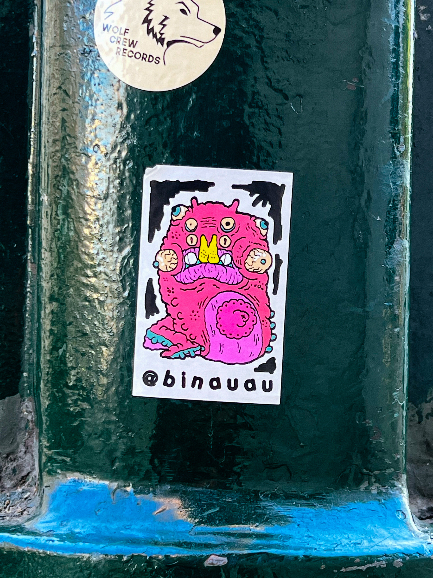 Sticker with a drawing of a very odd cartoony character. Plenty of eyes, pink. 