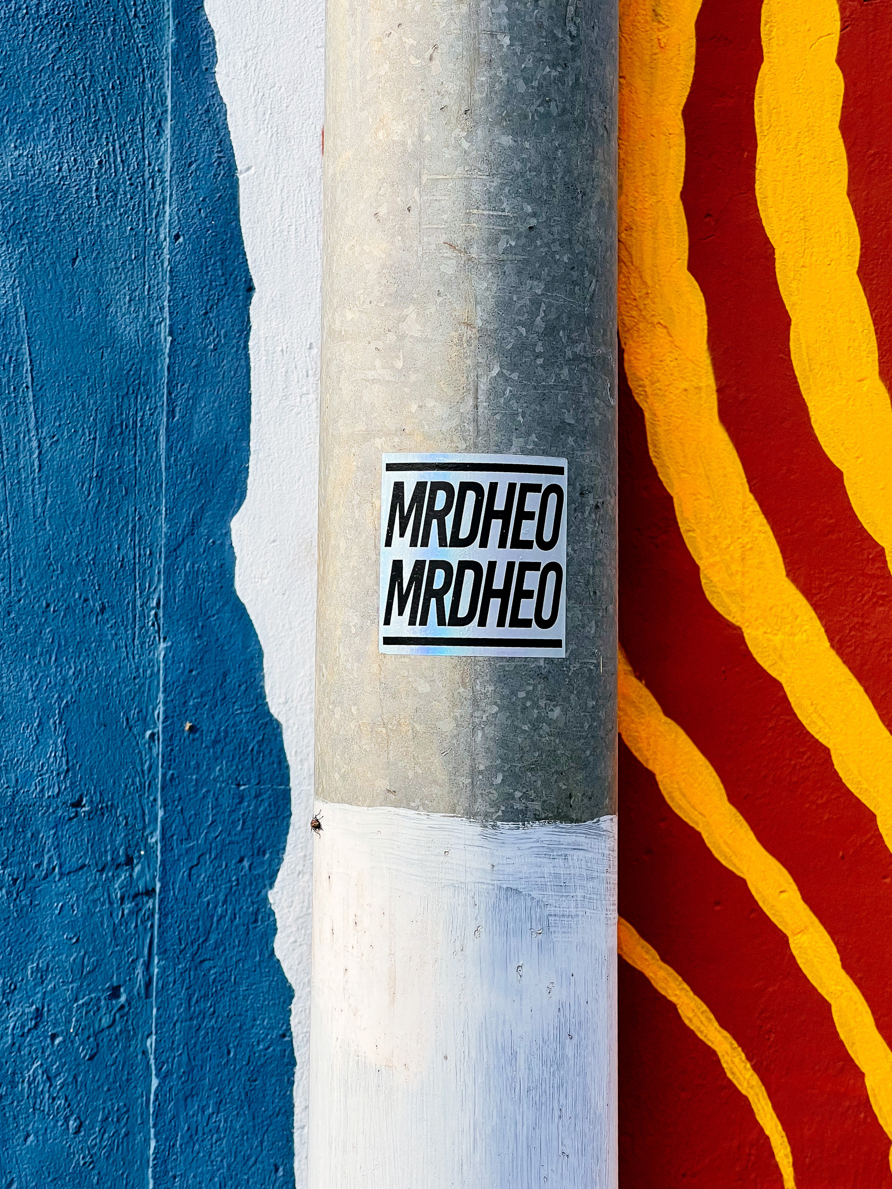 A sticker with the word “MRDHEO” written on it twice, and a graffitied wall. 