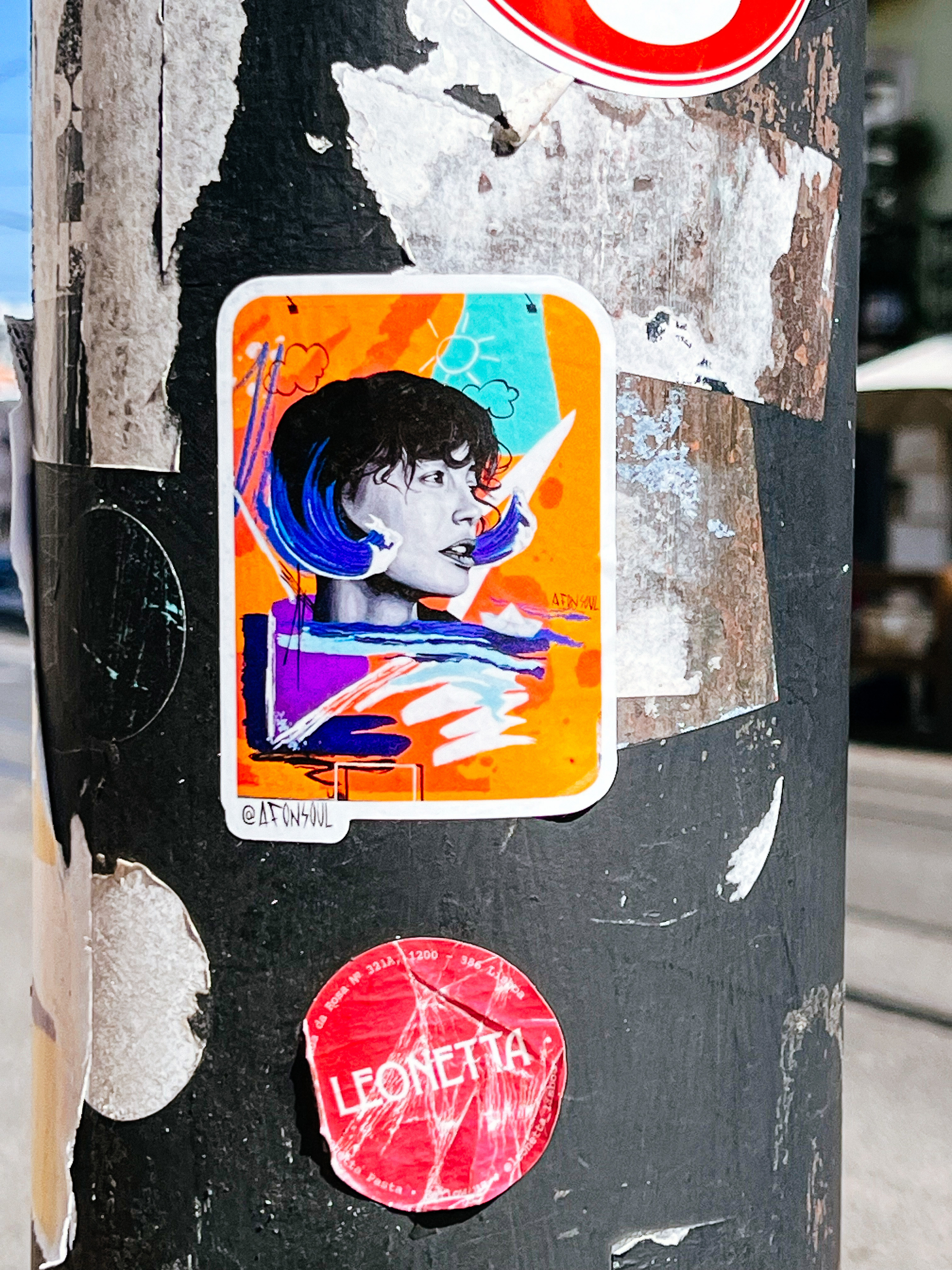Sticker with a woman’s face, orange background, and strokes of different colors around her face. 