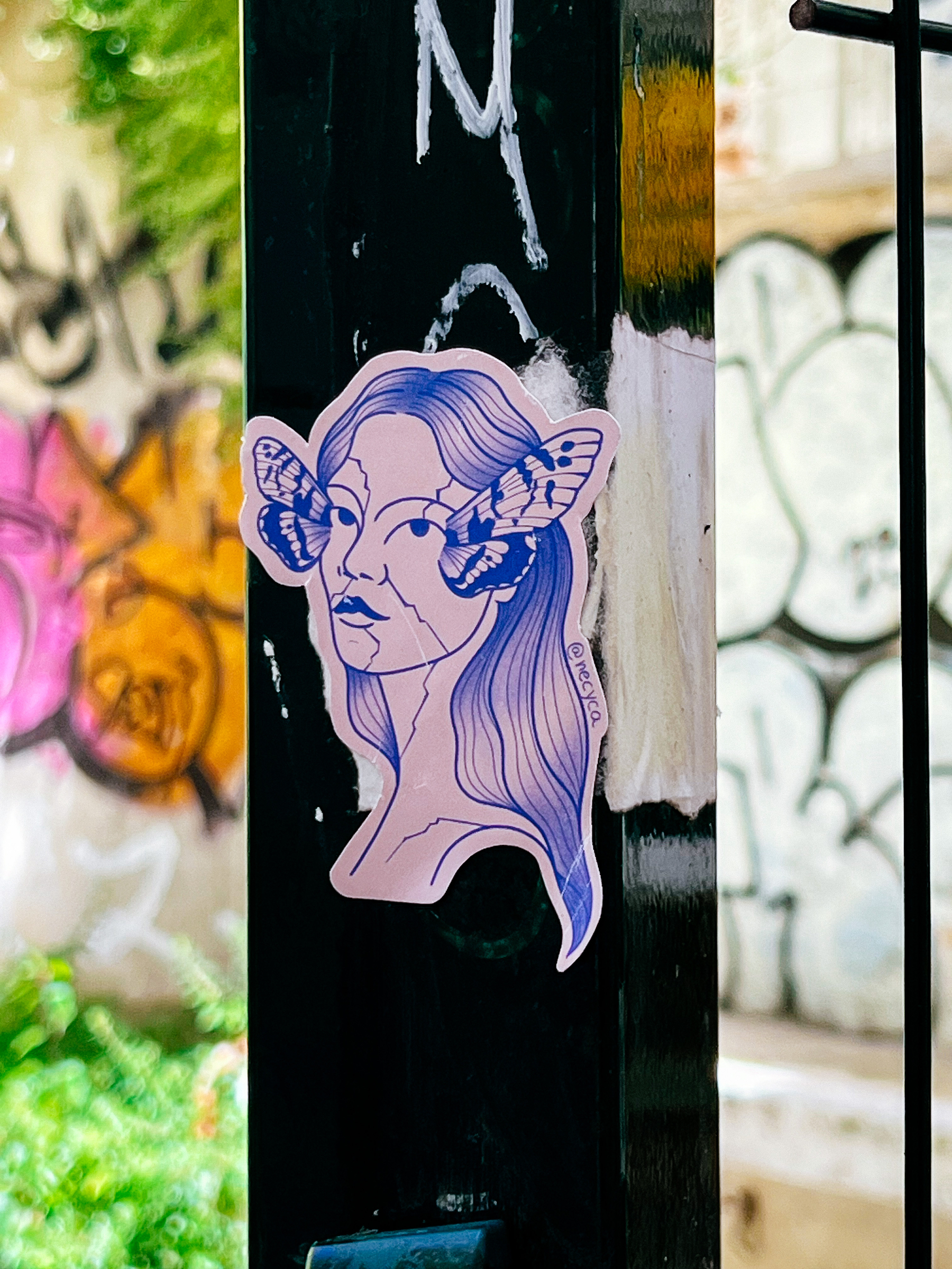 A woman’s face with butterfly wings next to her eyes. A sticker.  
