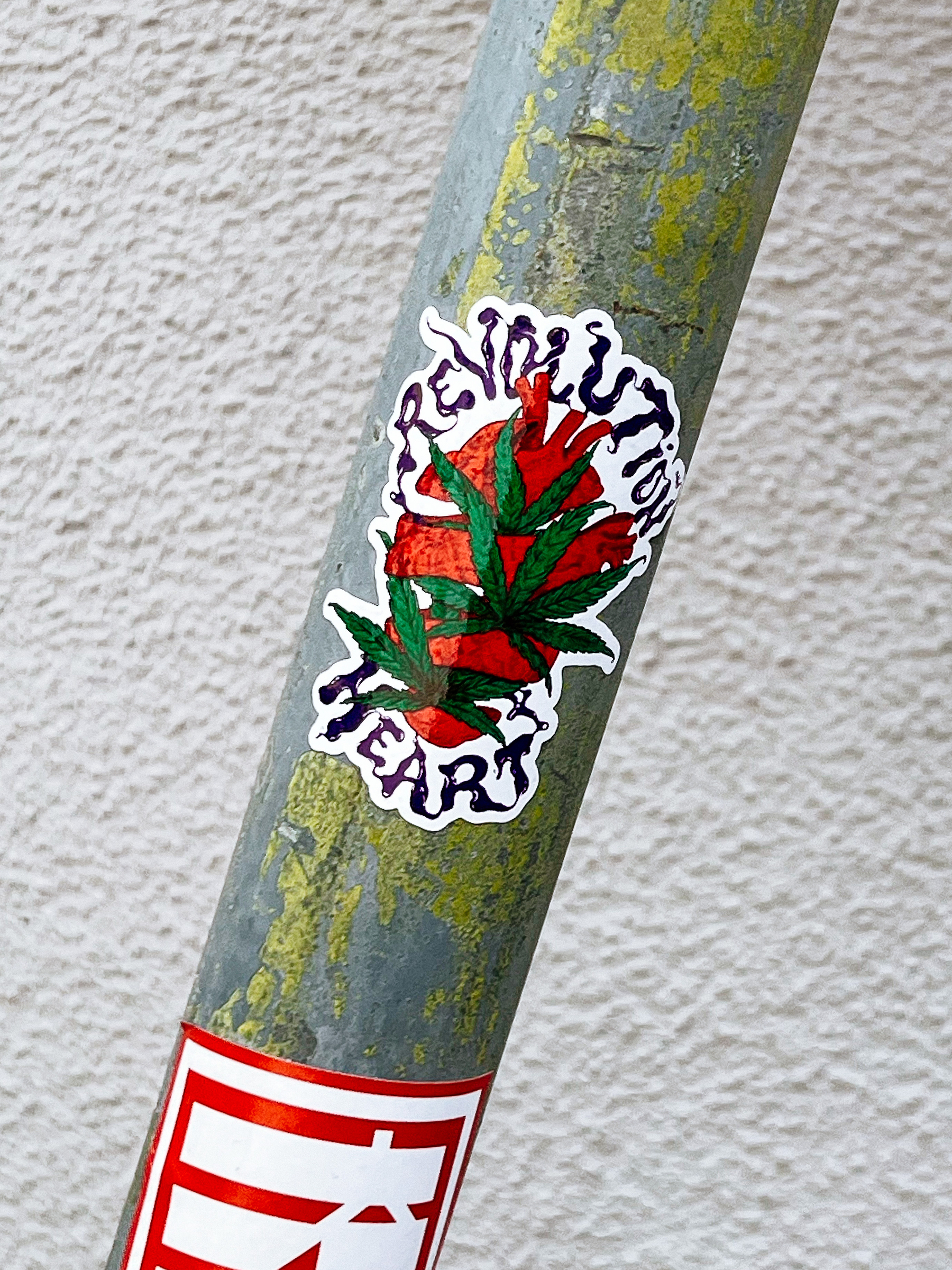 Sticker with the words “revolution heart”, and a drawing of a sliced heart with marijuana leaves. 