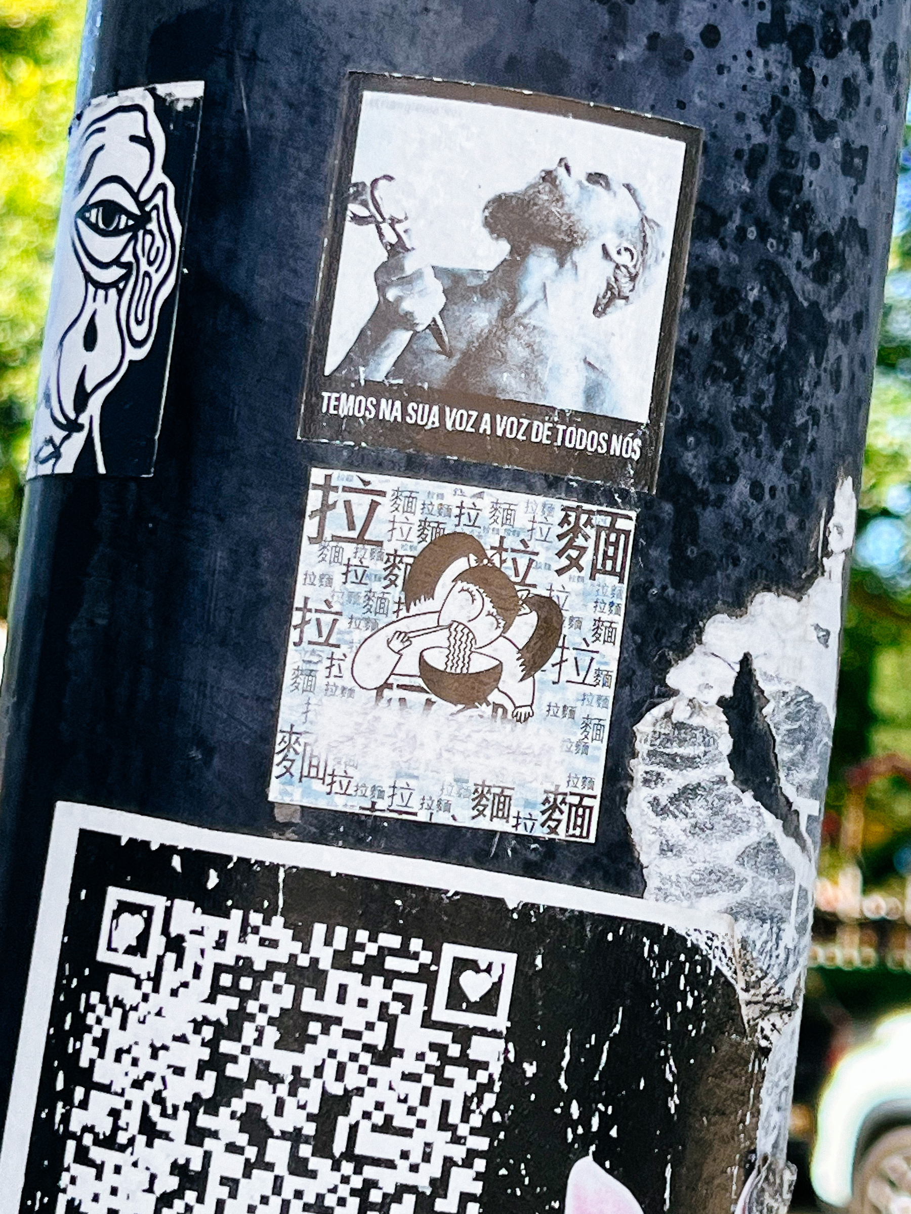 Several stickers on a lamp post. The central one has a drawing of a girl eating a bowl of ramen. 