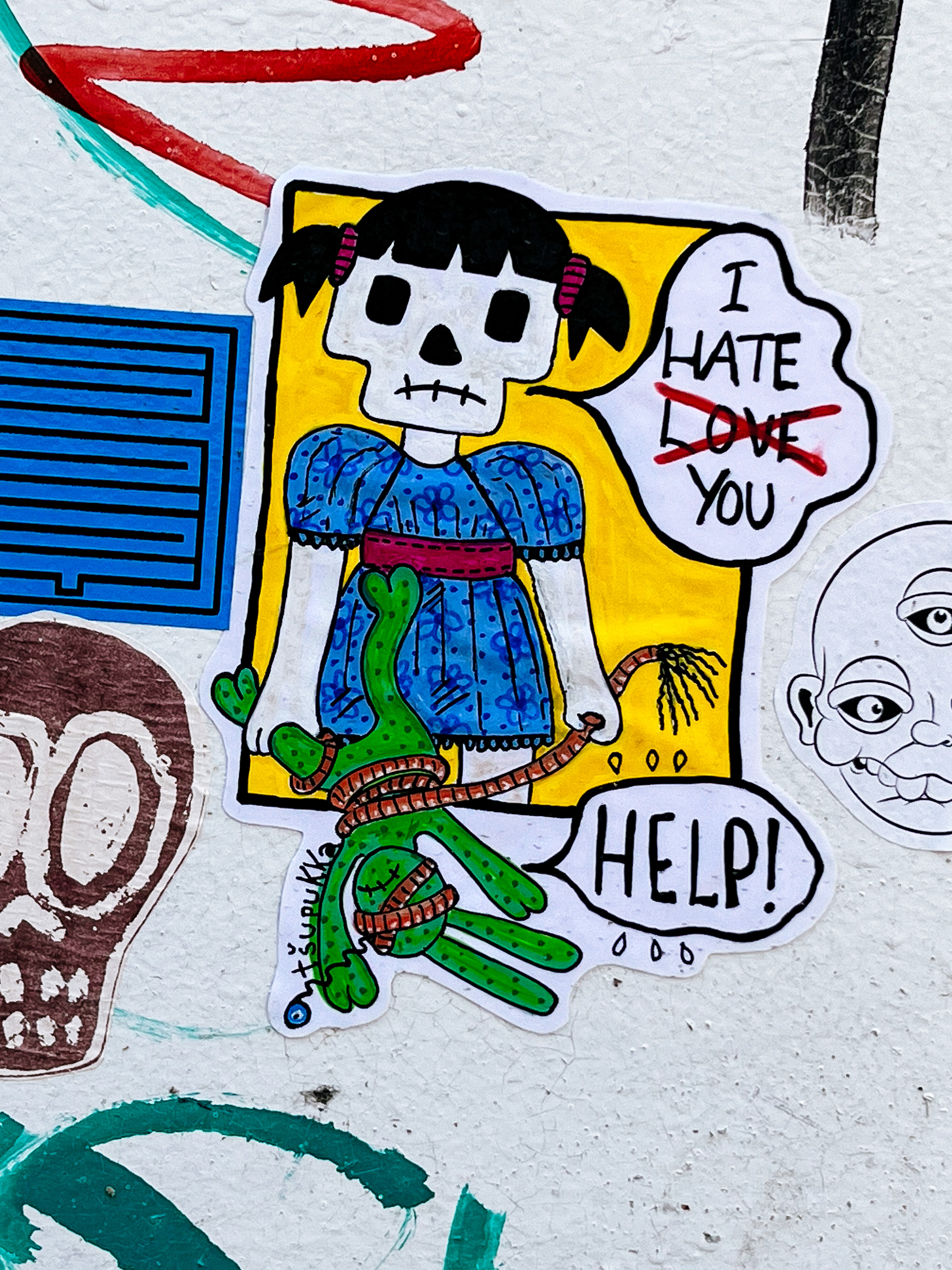 A girl with a skull for head holds a toy that has a whip wrapped around him, and he&rsquo;s calling for &ldquo;help&rdquo;. She&rsquo;s saying &ldquo;I hate you&rdquo;. It could say &ldquo;I love you&rdquo;, but the word &ldquo;Love&rdquo; has been crossed over. Sticker. 