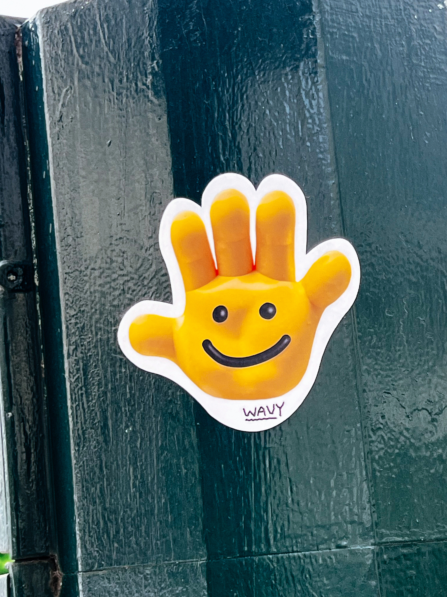A yellow, emoji-like hand, with a smile and two eyes drawn on it. Sticker. 