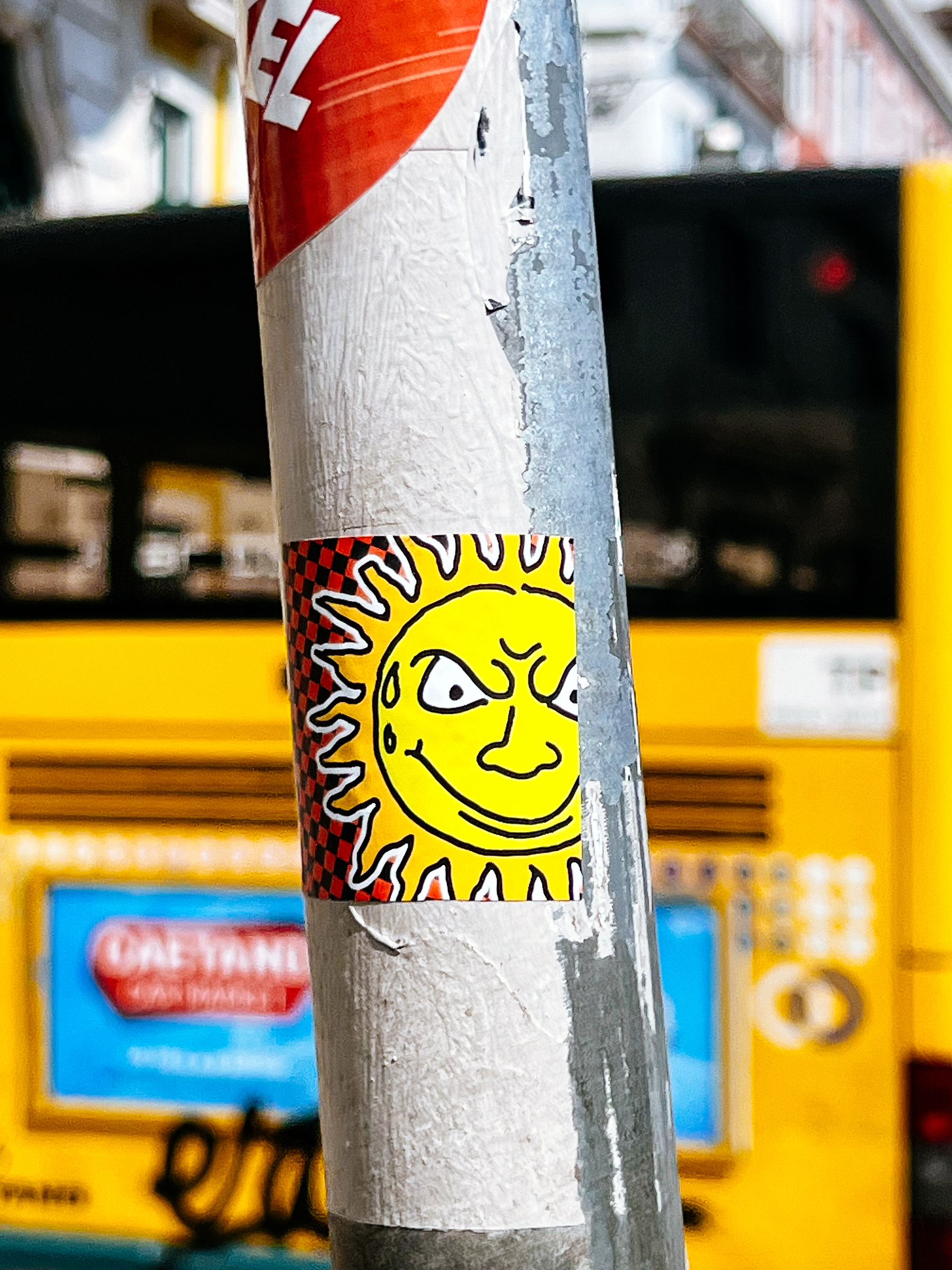 A mean looking sun in a sticker, with a very yellow bus in the background, out of focus. 