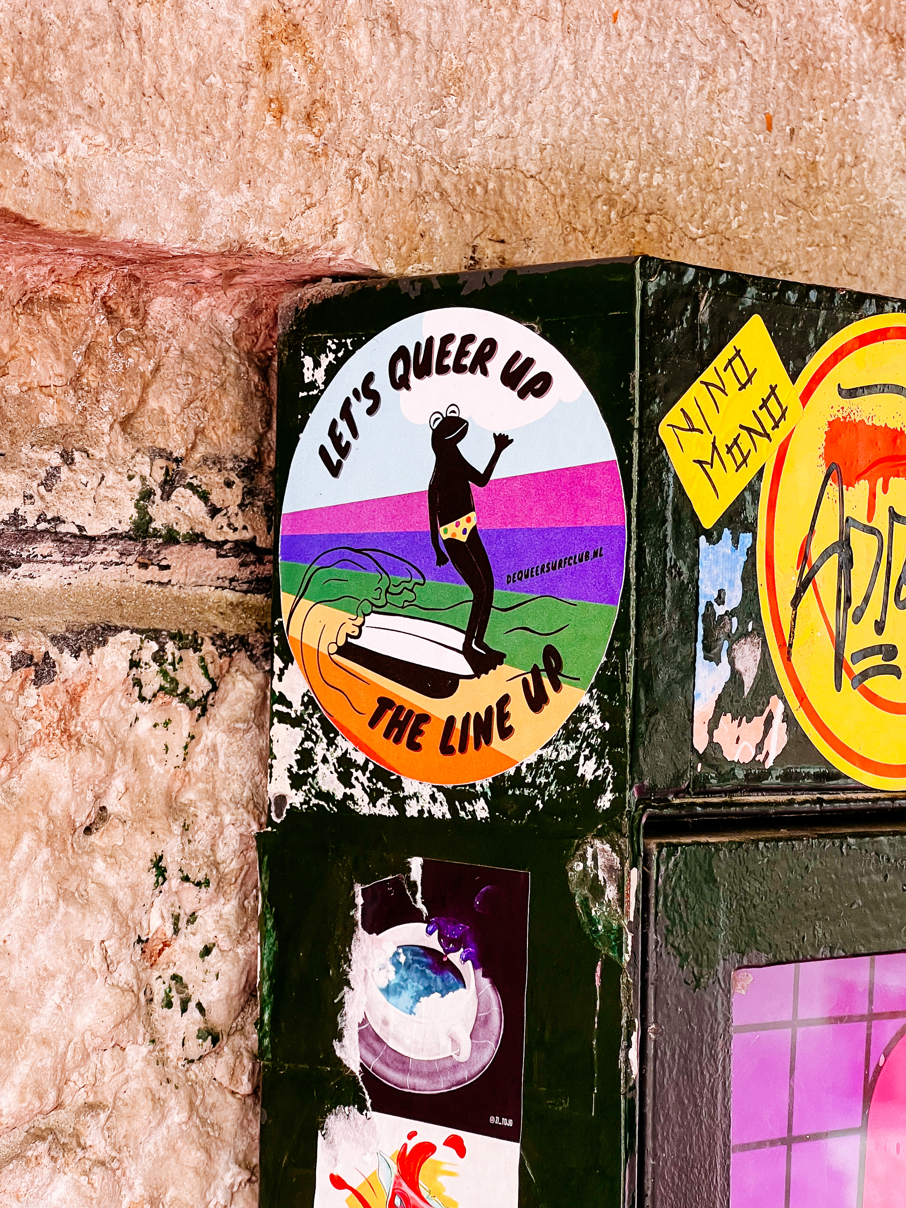 “Let’s queer up the line-up”, and a frog surfing a rainbow wave. A sticker. 